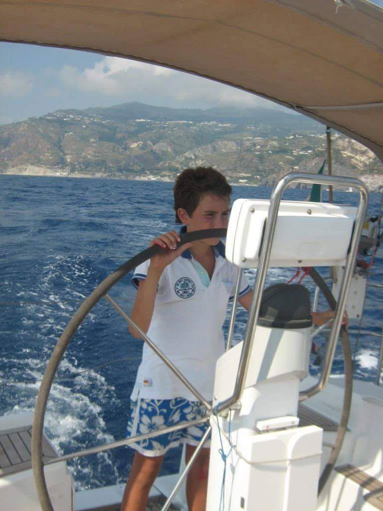 A boy at the helm of a sailing boat under way