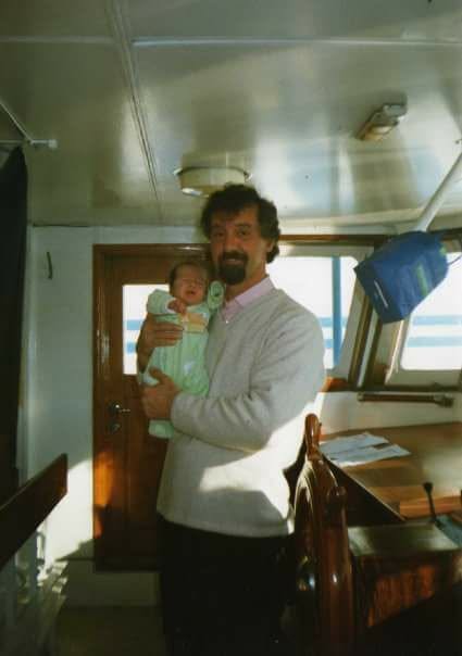 A newborn held by a man in the wheelhouse of a boat