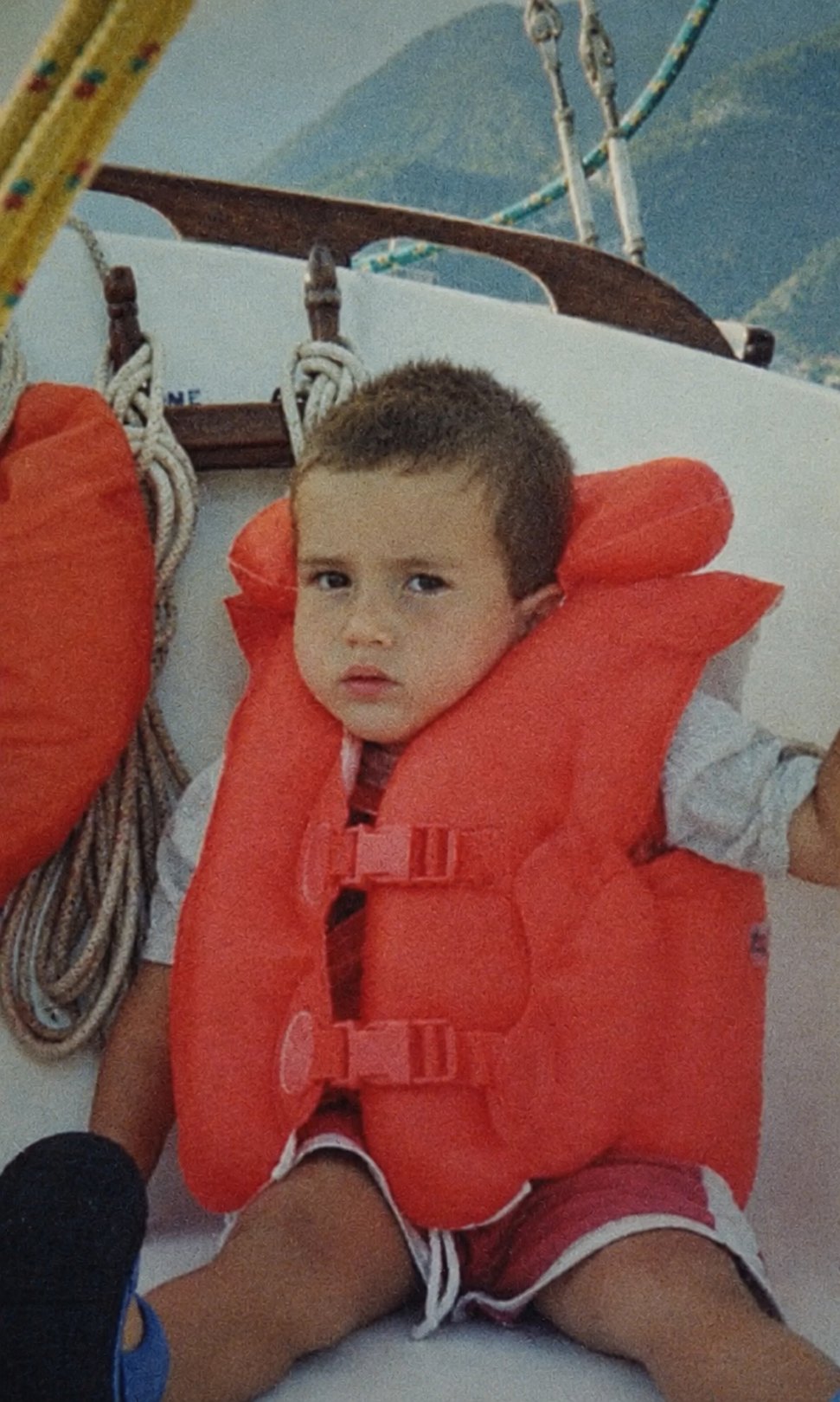 A child in an orange life jacket on board a sailing boat