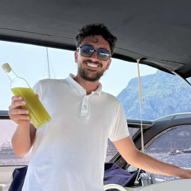 Giovanni smiling at the helm with a bottle of homemade limoncello